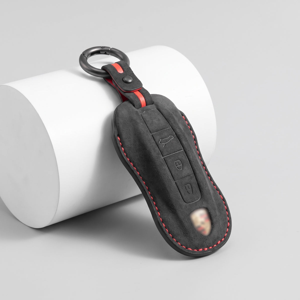 Black Alcantara key fob cover for Porsche with red contrast stitching, Type B, on a white display stand