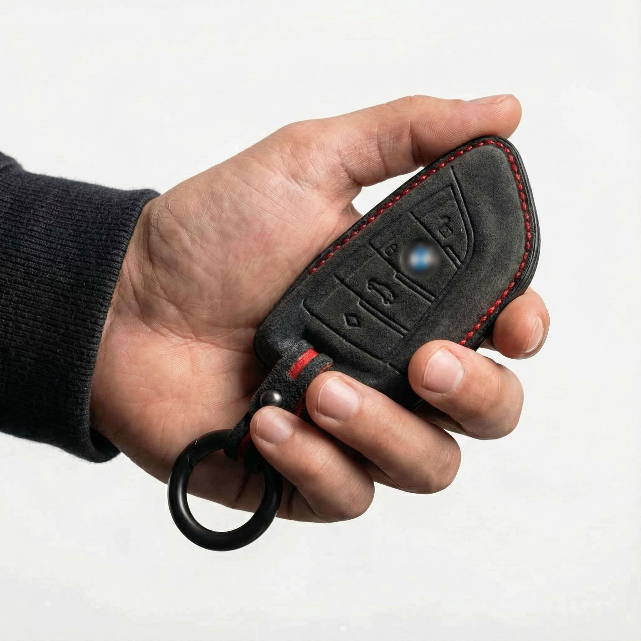 Hand holding a BMW key cover with a black alcantara cover on a white background