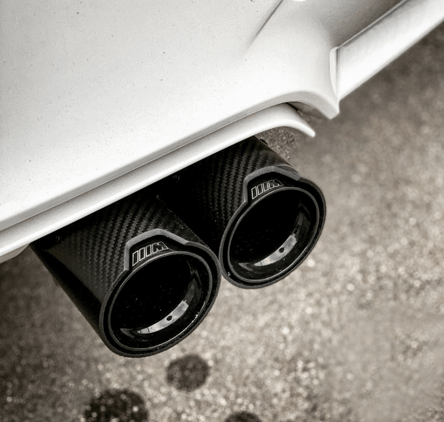 BMW M2 M3 M4 carbon fiber exhaust tips installed on a white BMW, showcasing a sleek, sporty design for enhanced vehicle performance and style