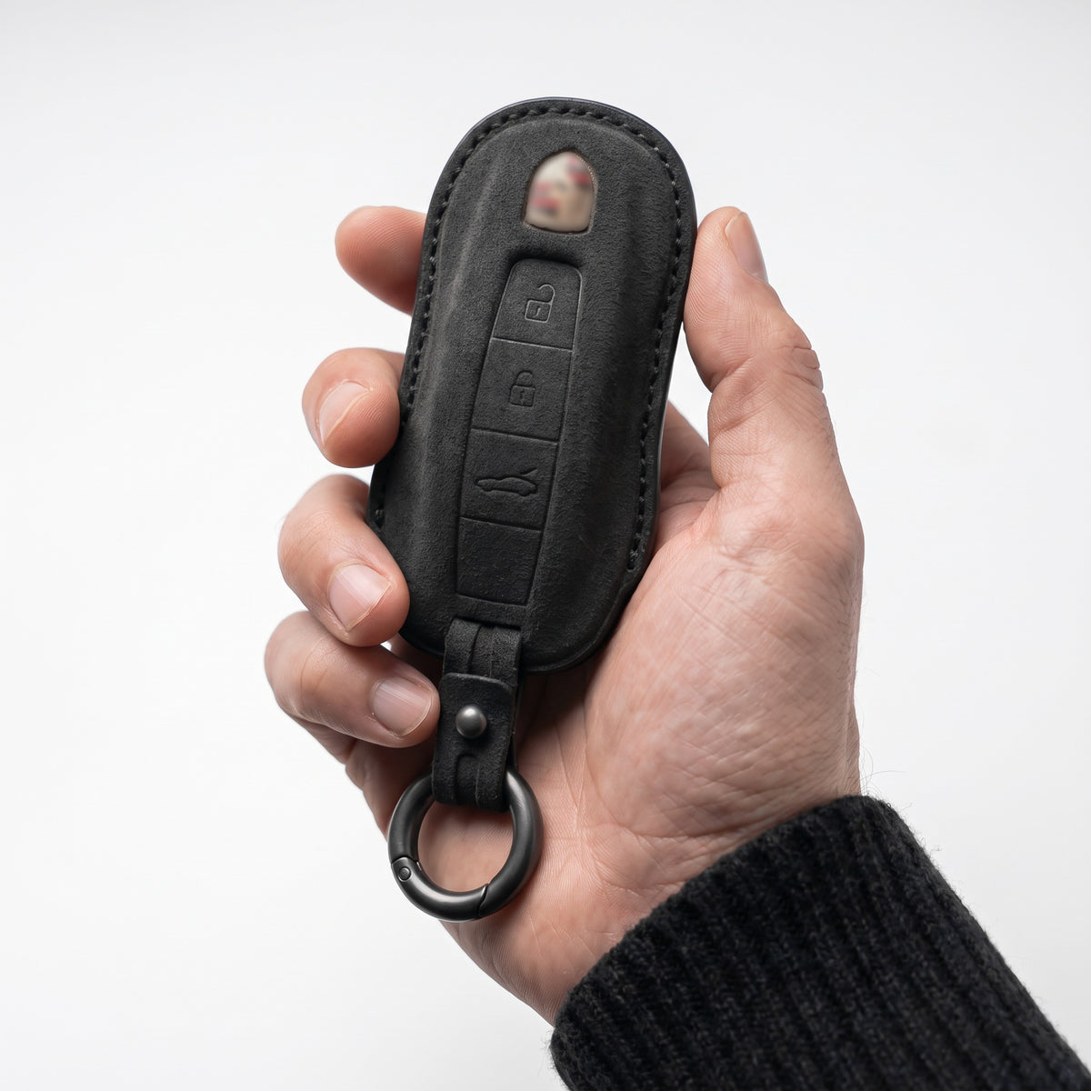 Hand holding a Porsche key in a black Alcantara cover with black stitching